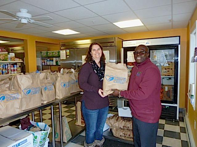 A man and a woman standing in a food pantry holding a Cleaning Authority Cares bag