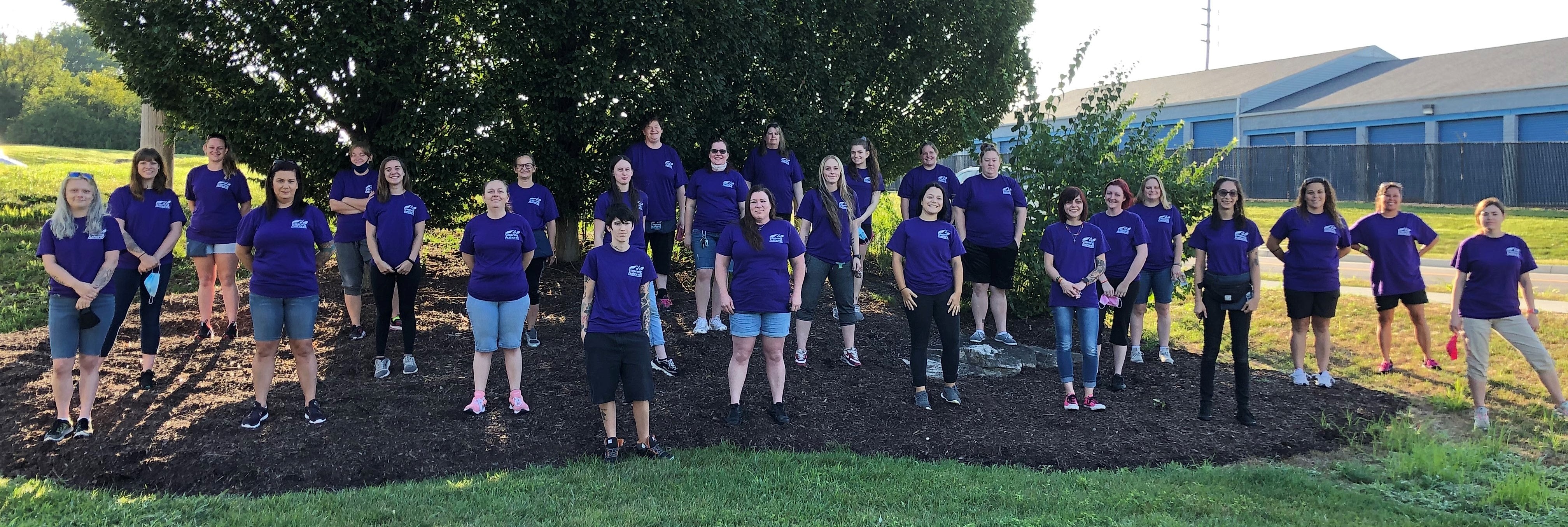 Team members from The Cleaning Authority in matching T-shirts stand on a hill in front of a tree.